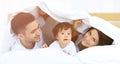 Happy family posing under a duvet while looking at the camera Royalty Free Stock Photo