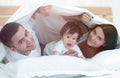 Happy family posing under a duvet while looking at the camera Royalty Free Stock Photo