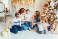 Happy family mother and five children relax playing near Christmas tree on Christmas eve at home. Mom daughters sons in