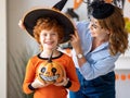 Happy family: mother laughs and helps the ginger son to put on a costume for the celebration of Halloween