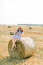 Happy family, mother and little daughter sitting on hay stack or bale in yellow wheat field in sunny summer day. Mommy Royalty Free Stock Photo