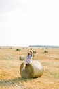 Happy family, mother and little daughter sitting on hay stack or bale in yellow wheat field in sunny summer day. Mommy Royalty Free Stock Photo