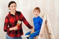 Repair in the apartment. Young family renovating their home together. Mother and kid paint a wall with a paint roller Royalty Free Stock Photo