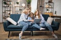 Happy family of mother and two cute daughters sitting together on comfortable couch, using laptop Royalty Free Stock Photo