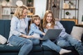 Happy family of mother and two cute daughters sitting together on comfortable couch, using laptop Royalty Free Stock Photo