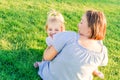 Happy family on nature. Mom and toddler baby daughter relaxing, hugging, laughing and have fun on green grass meadow at evening su Royalty Free Stock Photo