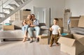 Happy family new home owners with child son in living room on moving day.