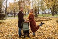 Happy family with a newborn baby in a stroller walking in an autumn park. Happy mother posing holding a stroller with a Royalty Free Stock Photo