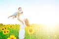 Happy family outdoors. Mother throws baby up, laughing and playing in the sunflowers field in summer on the nature Royalty Free Stock Photo