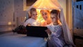 Happy family in pajamas sitting in tent in bedroom and using tablet computer. Family having time together, children with gadgets, Royalty Free Stock Photo