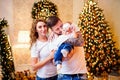 Happy family. Parents hugging little baby girl while standing near Christmas tree in living room Royalty Free Stock Photo