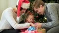 Happy family, parents showing Ney Year decorations to their cute child in front of Christmas tree. Mother in Santa hat Royalty Free Stock Photo