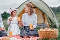 Happy family on picnic at camping. Mother and daughter eating near a tent in meadow or park Royalty Free Stock Photo