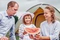 Happy family on picnic at camping. Mother, father and daughter eating watermelon near a tent in meadow or park Royalty Free Stock Photo