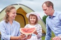 Happy family on picnic at camping. Mother, father and daughter eating watermelon near a tent in meadow or park Royalty Free Stock Photo