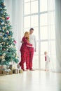 Happy family in plaid pajamas near the big window in the living room with a Christmas tree. Mother, father and little son waiting Royalty Free Stock Photo