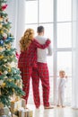 Happy family in plaid pajamas near the big window in the living room with a Christmas tree. Mother, father and little son waiting Royalty Free Stock Photo