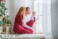 Happy family in plaid pajamas near the window in the living room with a Christmas tree. Mother, father and little son waiting for Royalty Free Stock Photo