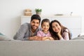 Happy family portrait. Happy arab mother, father and daughter cuddling and smiling to camera on couch at home