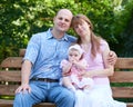 Happy family portrait with baby girl on outdoor, sit on wooden bench in city park, summer season, child and parent Royalty Free Stock Photo