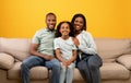 Happy family. Portrait of loving african american mother, dad and daughter sitting on sofa over yellow background Royalty Free Stock Photo