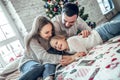 Happy family portrait of mother and girl child laying on cosy bed in festively decorated room with Christmas tree