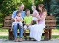 Happy family portrait on outdoor, group of five people sit on wooden bench in city park, summer season, child and parent Royalty Free Stock Photo