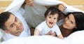 Happy family posing under a duvet while looking at the camera Royalty Free Stock Photo