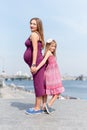 Happy family, pregnant mother and her daughter little girl child walking and hugging on the embankment in the summer day Royalty Free Stock Photo