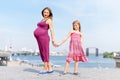 Happy family, pregnant mother and her daughter little girl child walking and hugging on the embankment in the summer day Royalty Free Stock Photo