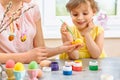 Happy family preparing for Easter and painting Easter eggs, little girl with a smile paint egg carefully