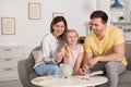 Happy family putting coin into piggy bank at table indoors. Royalty Free Stock Photo