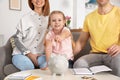 Happy family putting coin into piggy bank at table. Saving money Royalty Free Stock Photo