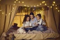 Happy mother and children sitting in playroom tent and reading book of fairy tales
