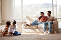 Happy family relaxing at home. Smiling young parents with girls on a sofa, watching their cute little children play and Royalty Free Stock Photo