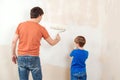 Happy family renovating their new home. Father showing his son how painting wall with a roller Royalty Free Stock Photo