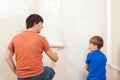 Happy family renovating their new home. Father showing his son how painting wall with a roller Royalty Free Stock Photo