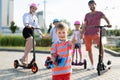 Happy family rides electric scooters and gyroscuters in the park, in the foreground a small boy holds a skate in his Royalty Free Stock Photo