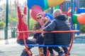 Happy family riding a carousel, spinning in a metal roundabout equipment at a playground on a sunny autumn day.