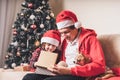 Happy family in Santa hat, father and child boy open Christmas gift at home. Sitting on a couch in the living room with Royalty Free Stock Photo