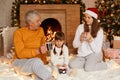 Happy family senior man, woman and little girl sitting in festive room near fireplace and christmas tree and drinking hot tree, Royalty Free Stock Photo