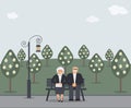 Happy family seniors: cute smiling elderly man and woman with clutch bag are sitting on bench in park. Retired elderly couple in