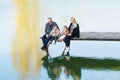 Happy family sit on the pier in warm autumn day dangling his legs in the water. Royalty Free Stock Photo