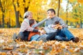 Happy family sitting on fallen leaves, playing and having fun in autumn city park. Children and parents together having a nice day Royalty Free Stock Photo