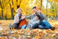 Happy family sitting on fallen leaves, playing and having fun in autumn city park. Children and parents together having a nice day Royalty Free Stock Photo