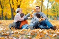 Happy family sitting on fallen leaves, playing and having fun in autumn city park. Children and parents together having a nice day Royalty Free Stock Photo
