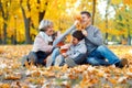 Happy family sitting on fallen leaves, playing and having fun in autumn city park. Children and parents together having a nice day Royalty Free Stock Photo