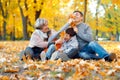 Happy family sitting on fallen leaves, playing and having fun in autumn city park. Children and parents together having a nice day Royalty Free Stock Photo