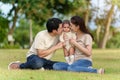 happy family sitting on a green grass filed. father and mother kissing their infand baby in park