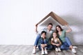 Happy family sitting under cardboard roof near wall, space for text. Insurance concept